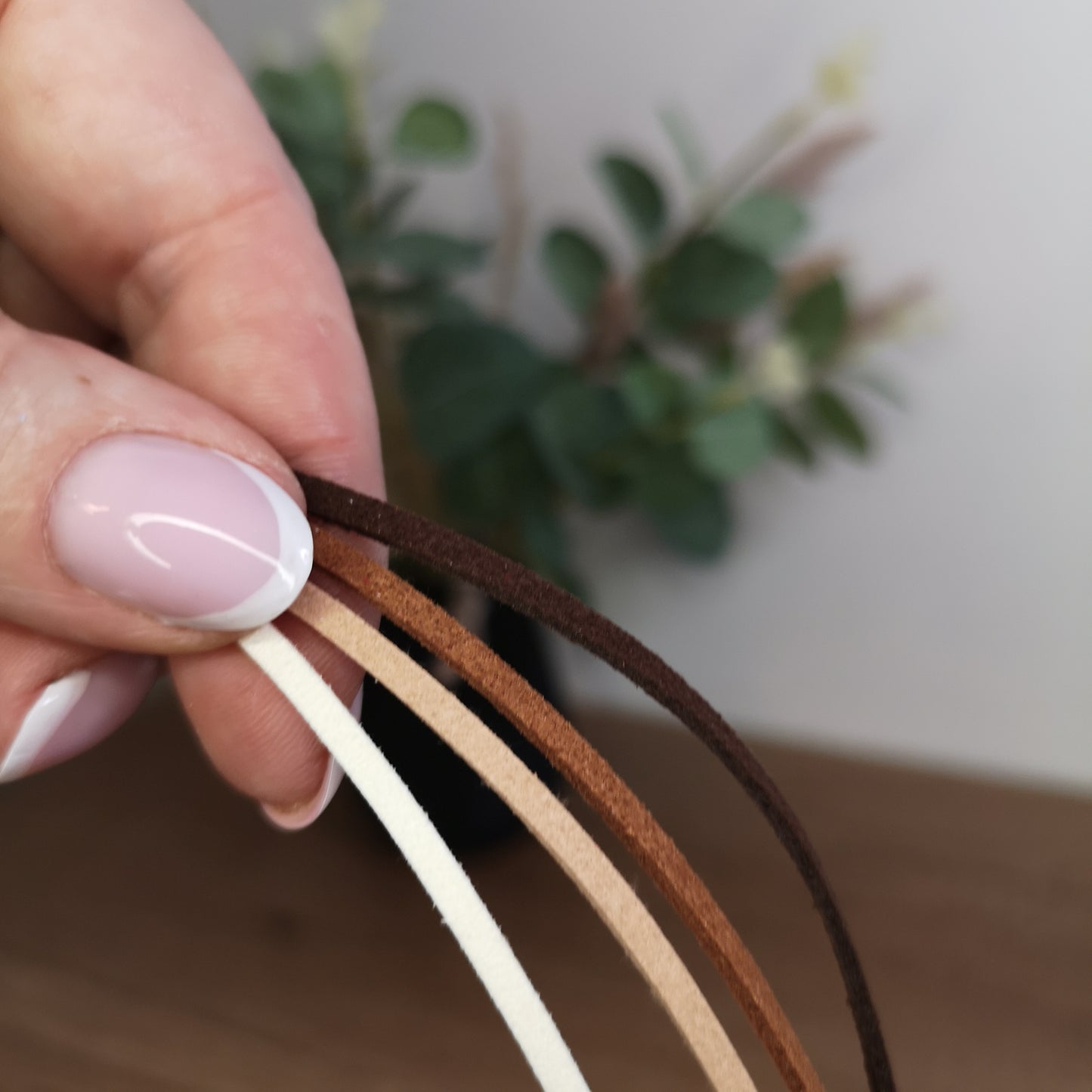 Hand holding three leather straps of different colors against a blurred plant background