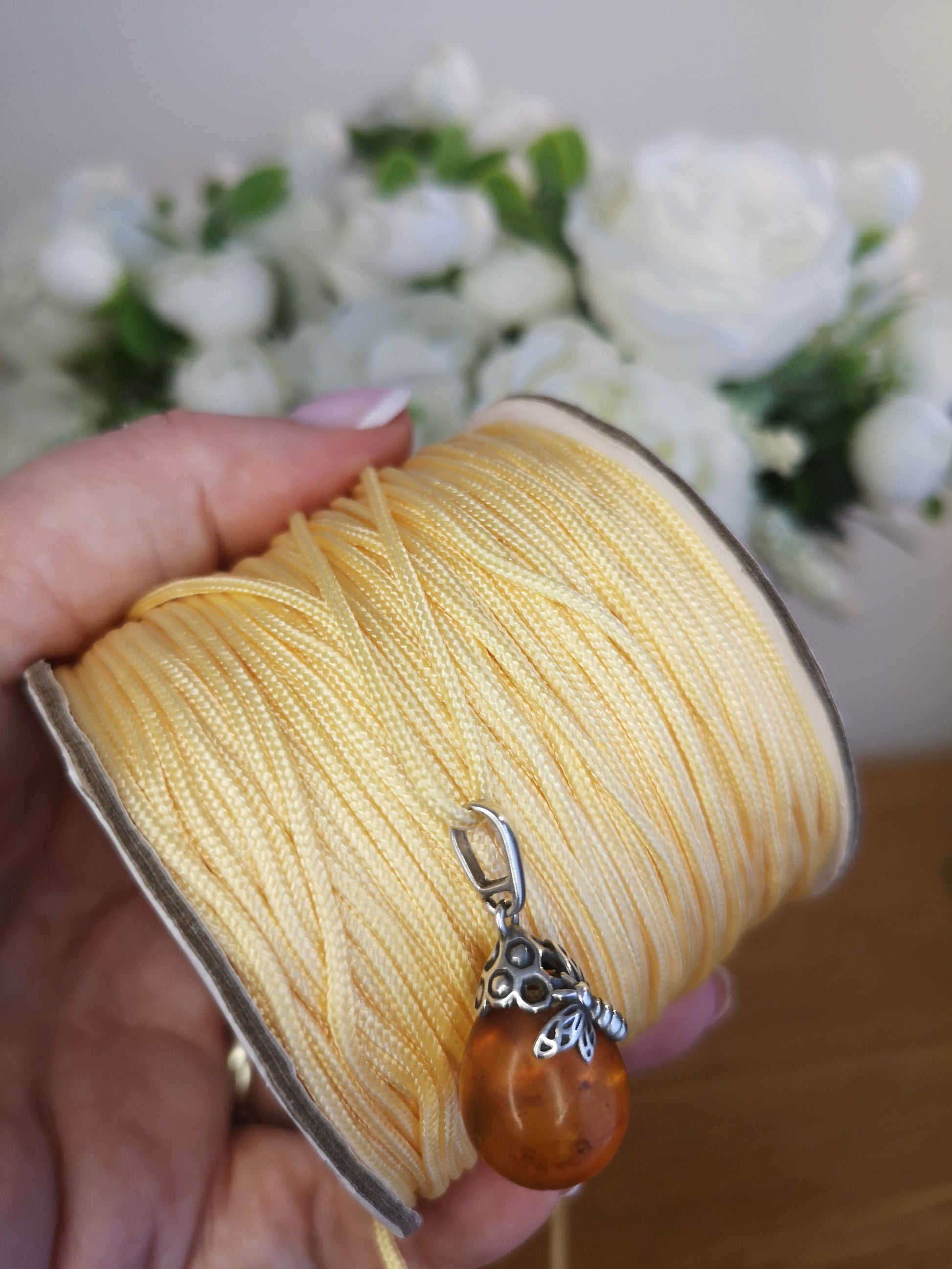 Spool of yellow thread with a pendant held by a hand, flowers in the background