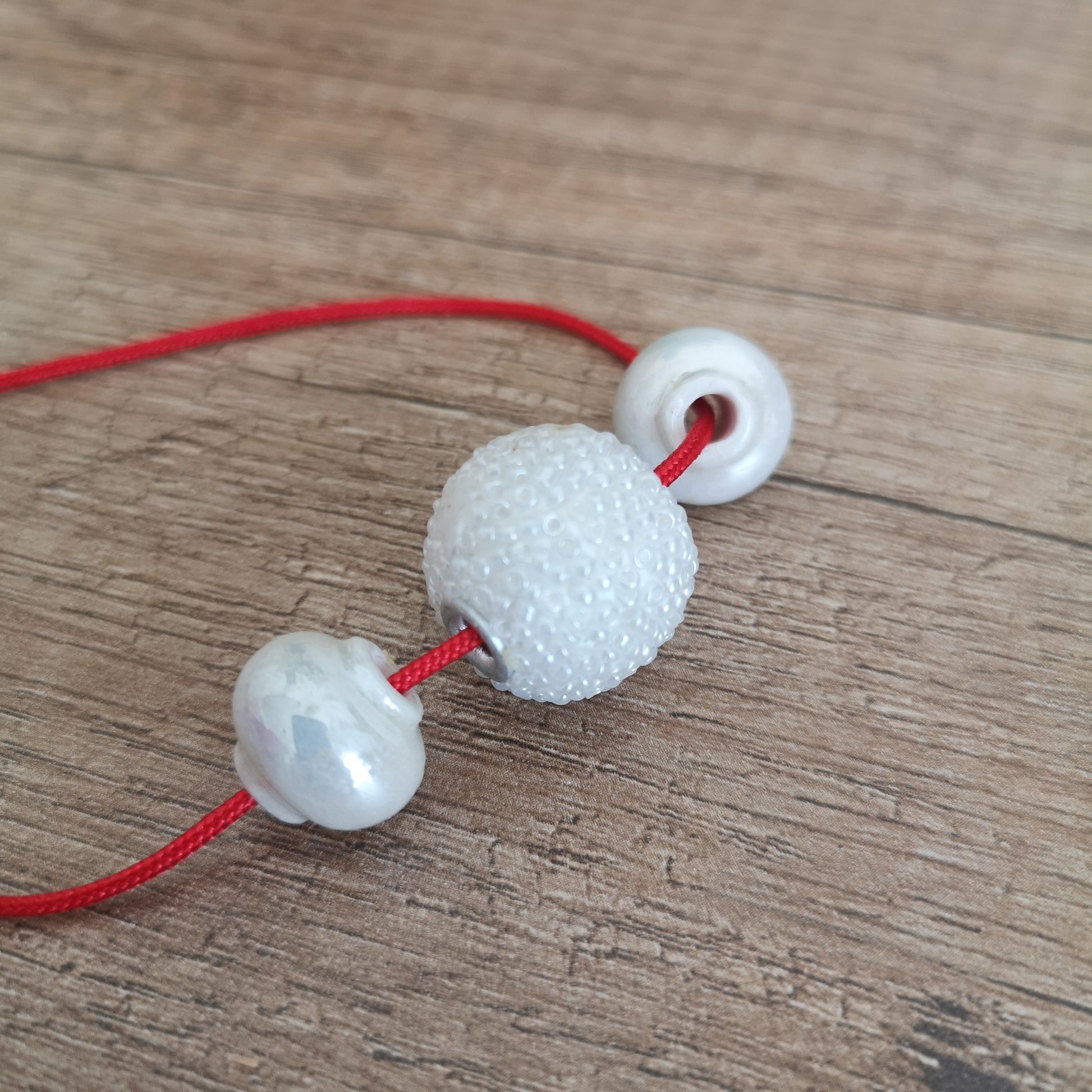 Three white beads on a red string against a wooden background