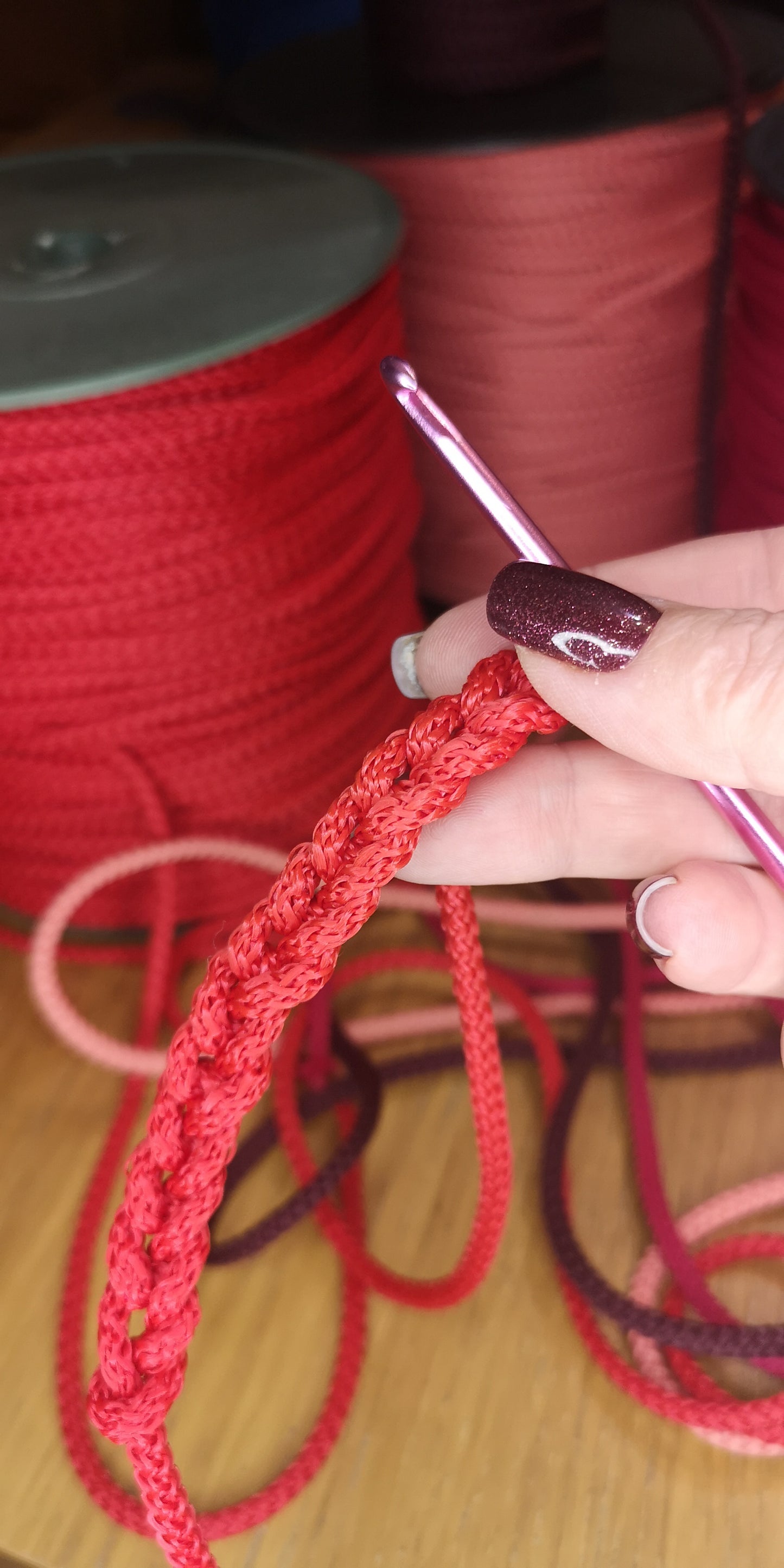 Person holding a crochet hook with red yarn, with spools of yarn in the background.