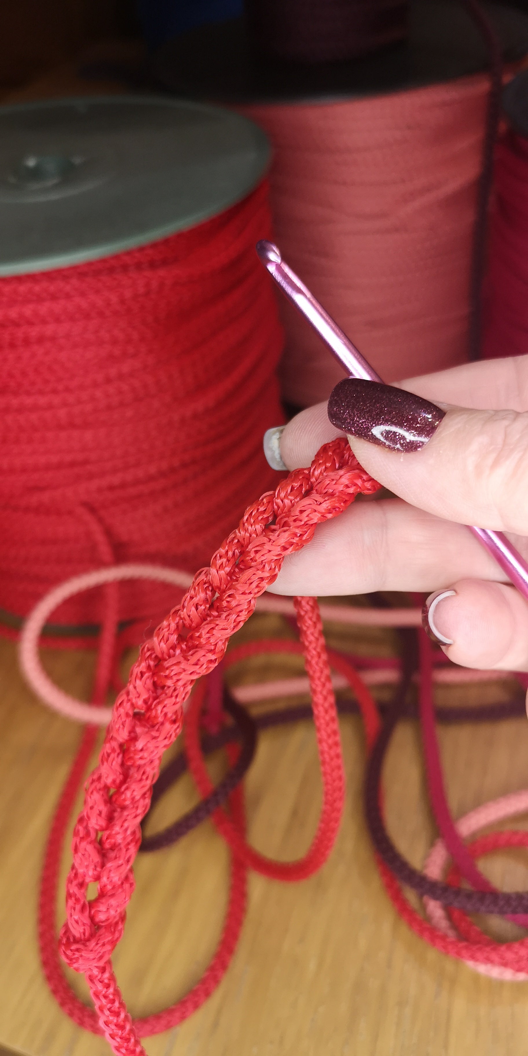 Person holding a crochet hook with red yarn, with spools of yarn in the background.