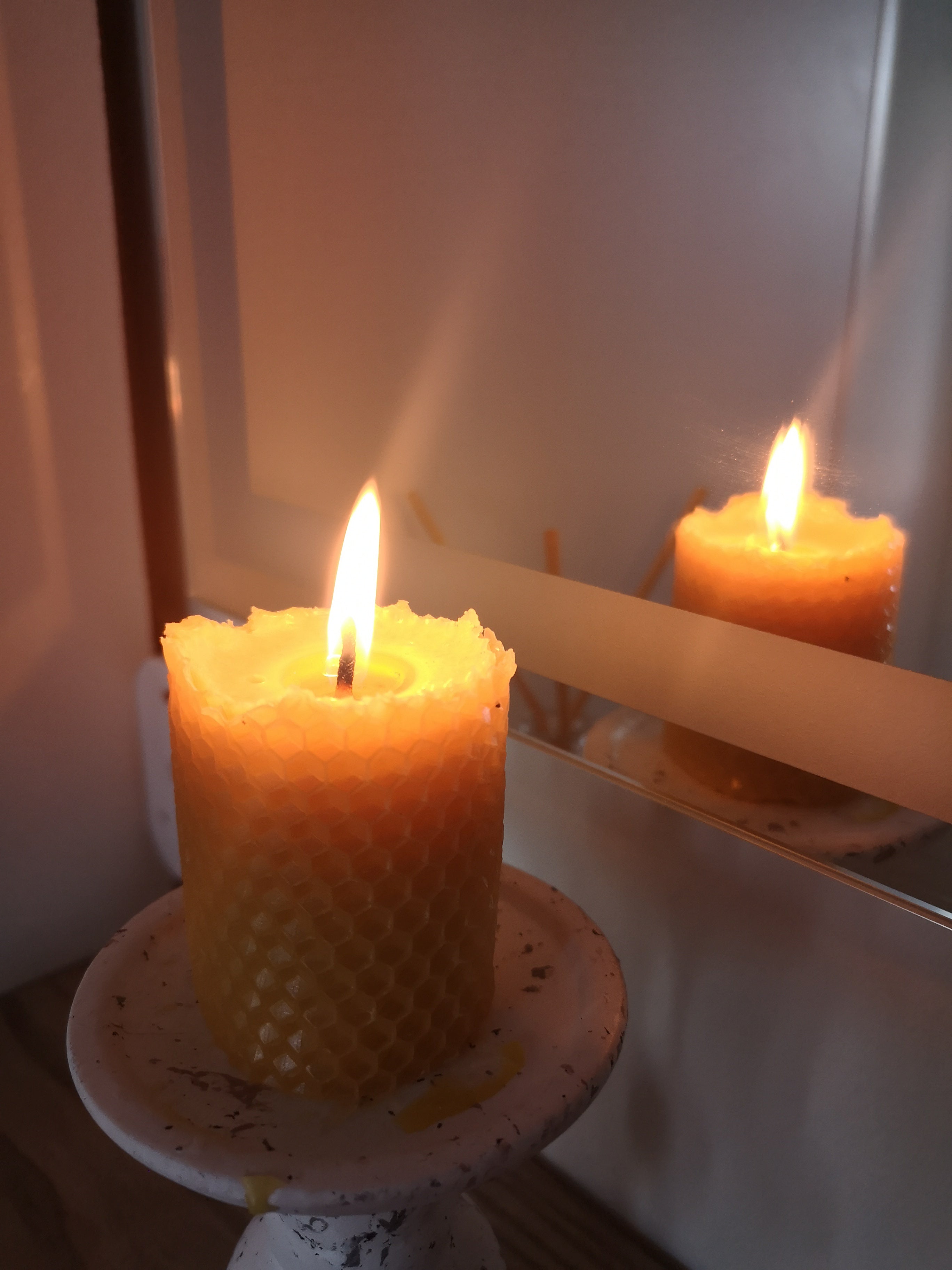 Burning beeswax candle next to mirror