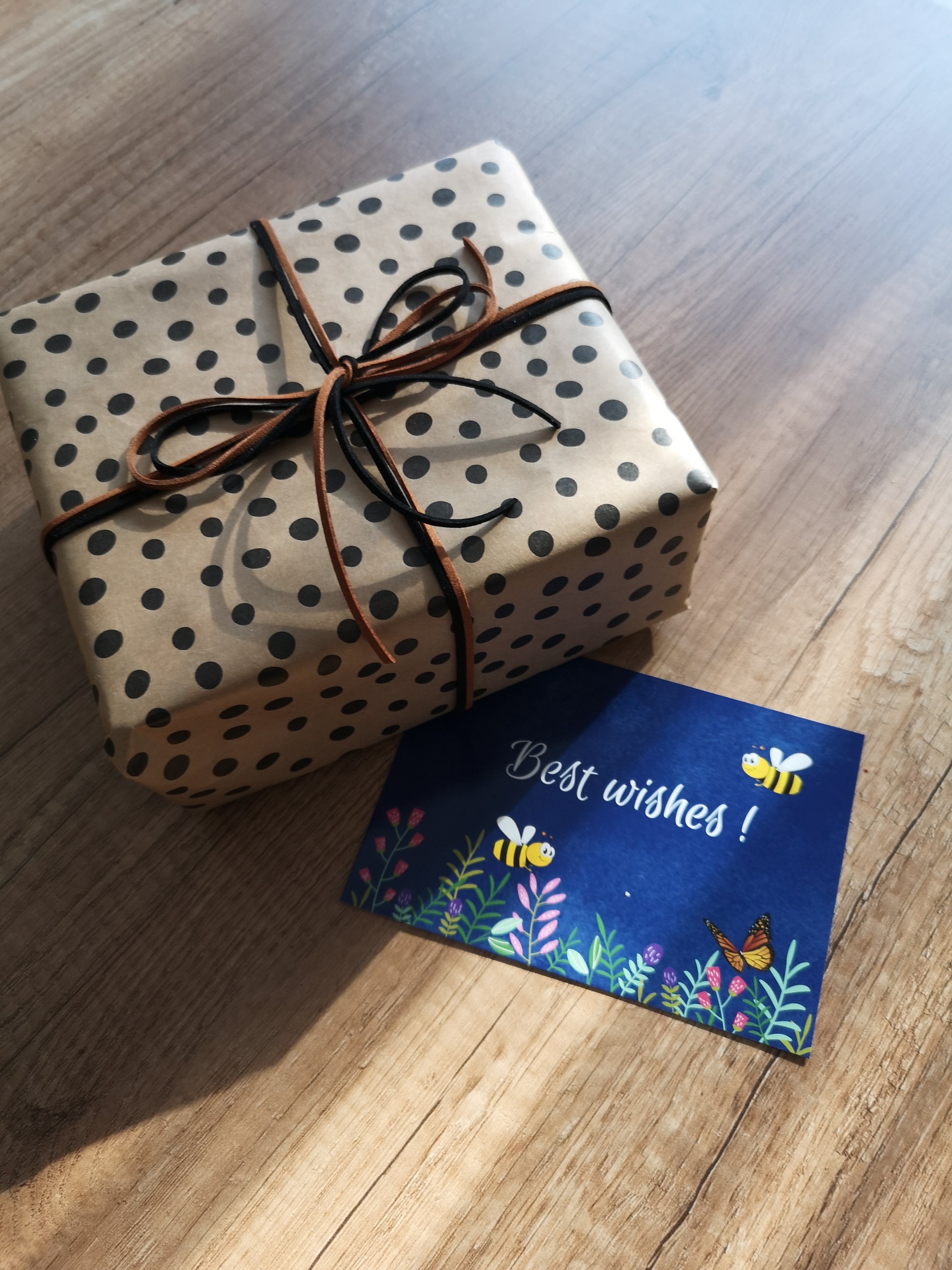 Gift wrapped in polka dot paper with brown ribbon on a wooden surface, accompanied by a 'Best wishes!' card.