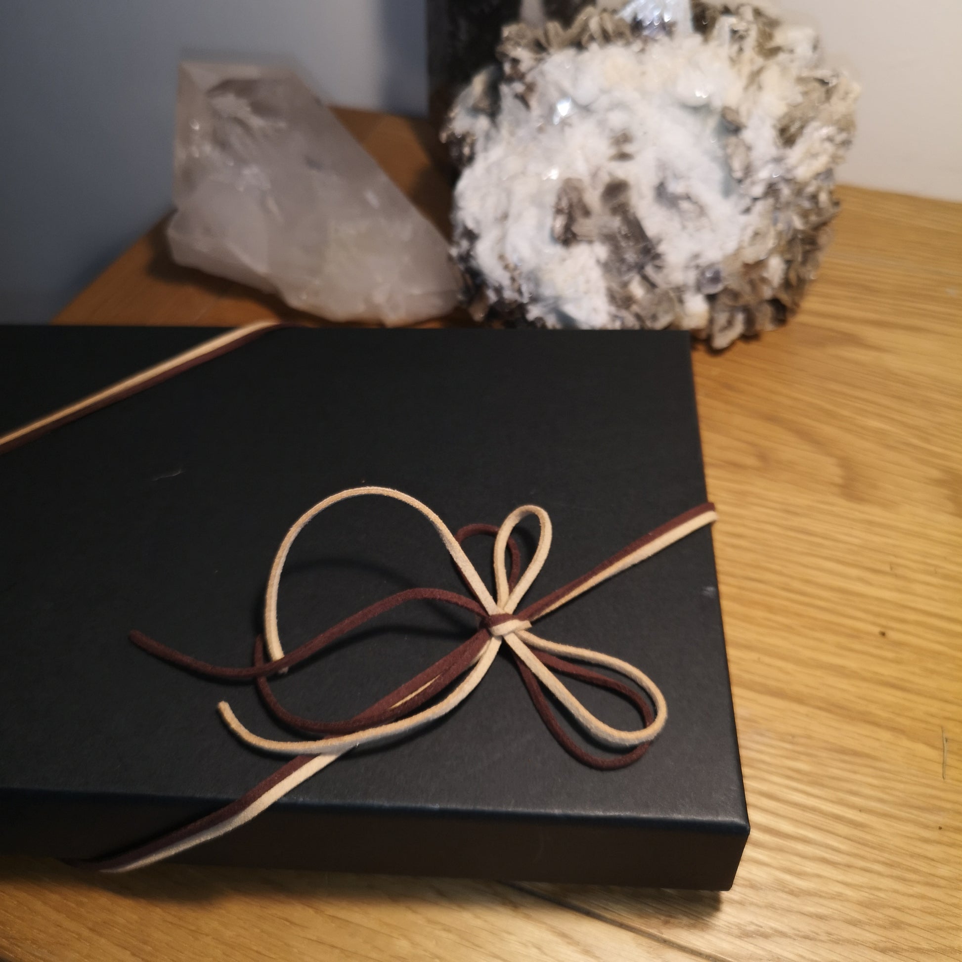 Black box with brown ribbon on a wooden surface with crystals in the background